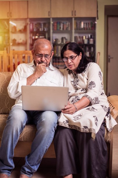 Senior indisch / asiatisches Paar Buchhaltung, Hausfinanzierung und Rechnungen prüfen mit Laptop, Taschenrechner und Geld, während zu Hause im Garten sitzen - Foto, Bild