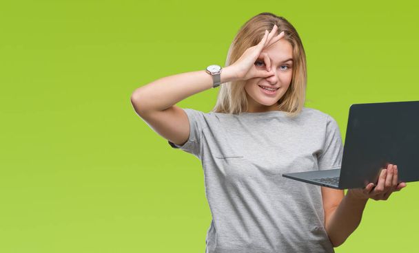 Young caucasian woman using computer laptop over isolated background with happy face smiling doing ok sign with hand on eye looking through fingers - Photo, image