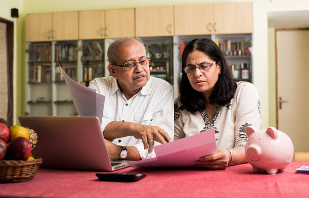 Старшие индийско / азиатская пара бухгалтерский учет, ведение домашнего финансирования и проверка счетов с ноутбука, калькулятора и денег, сидя в саду
 - Фото, изображение