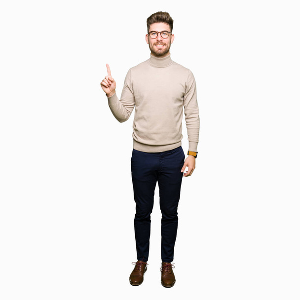 Young handsome business man wearing glasses showing and pointing up with finger number one while smiling confident and happy. - Photo, Image