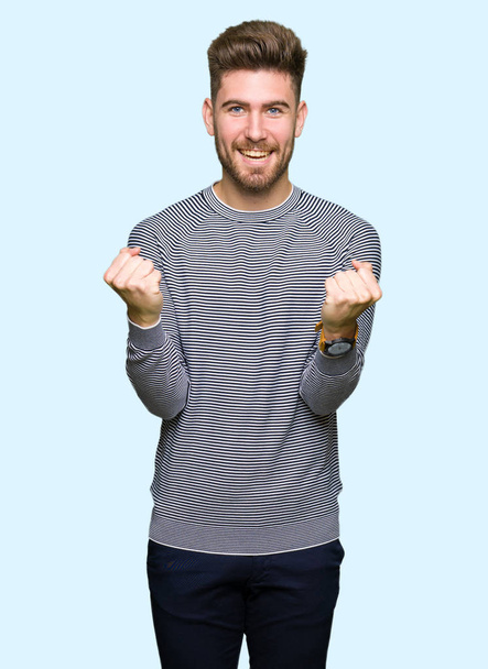 Молодий красивий чоловік у смужках светр святкує здивований і вражений успіхом з піднятими руками і відкритими очима. концепція переможця
. - Фото, зображення