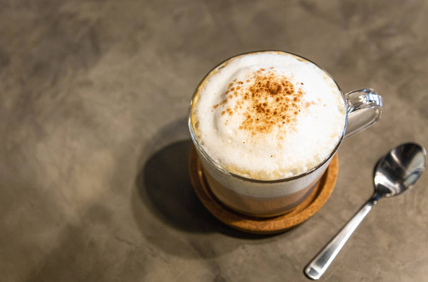 Cappuccino café quente com espuma de leite tampa na parte superior,, polvilhado com chocolate em pó ou canela, no fundo de cimento no café pela manhã
 - Foto, Imagem