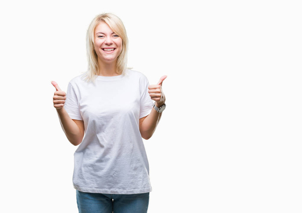 Young beautiful blonde woman wearing white t-shirt over isolated background success sign doing positive gesture with hand, thumbs up smiling and happy. Looking at the camera with cheerful expression, winner gesture. - 写真・画像