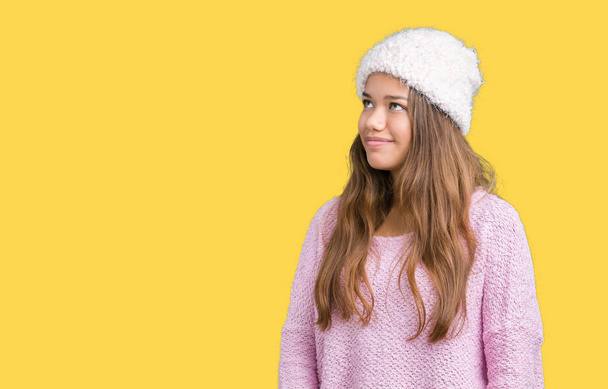 Młoda piękna kobieta brunetka na sobie sweter i czapka zimowa na na białym tle, tło patrząc od strony z uśmiechem na twarzy, naturalny wyraz. Śmiejąc się pewnie. - Zdjęcie, obraz