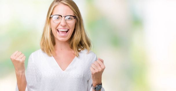 Beautiful young woman wearing glasses over isolated background celebrating surprised and amazed for success with arms raised and open eyes. Winner concept. - Foto, afbeelding