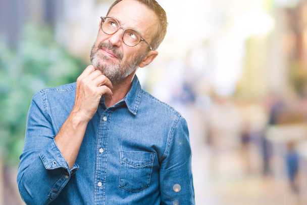 Middle age hoary senior man wearing glasses over isolated background with hand on chin thinking about question, pensive expression. Smiling with thoughtful face. Doubt concept. - Foto, immagini