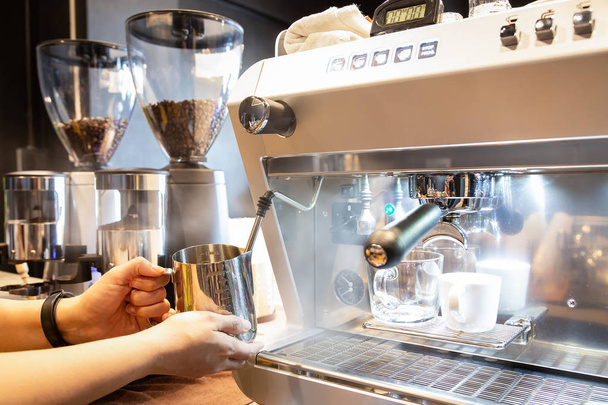 女性両手ステンレス ミルク ピッチャー、少女バリスタのコーヒー ショップでコーヒー マシンと熱いカプチーノ用ステンレス製ミルク ピッチャーにミルクを蒸し - 写真・画像