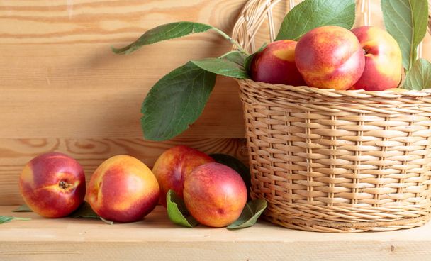 Nectarines in a wicker basket on a wooden table. - Photo, Image