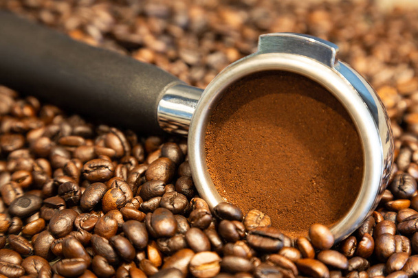 Portafilter sur fond de grains de café, grains de café torréfiés de torréfacteur, poudre de café dans le portafilter, préparer de l'espresso le matin au café
    - Photo, image