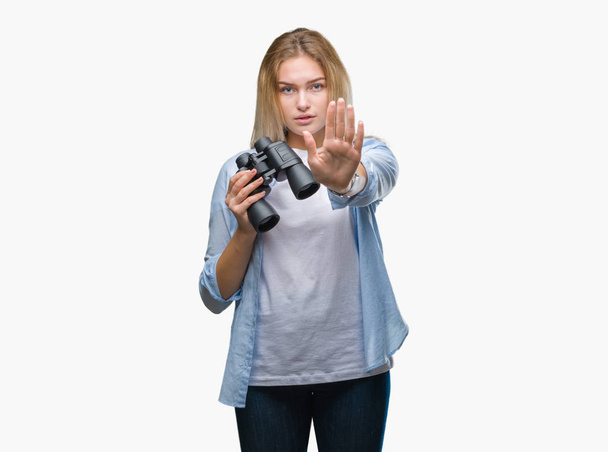 Jeune femme caucasienne tenant des jumelles sur fond isolé avec la main ouverte faisant stop signe avec expression sérieuse et confiante, geste de défense
 - Photo, image