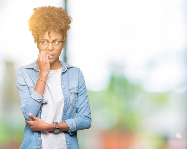 Kaunis nuori afrikkalainen amerikkalainen nainen yllään lasit yli eristetty tausta näyttää stressaantunut ja hermostunut kädet suulla puree kynnet. Ahdistuneisuusongelma
. - Valokuva, kuva