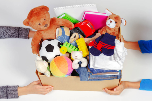 Concept de don. Mains d'enfant avec boîte de don avec vêtements, livres, fournitures scolaires et jouets, fond blanc
 - Photo, image