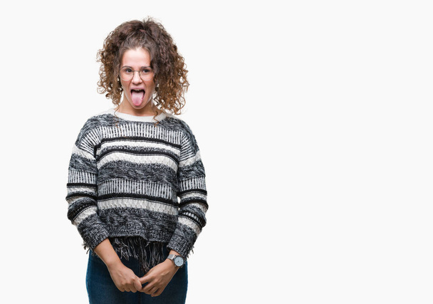 Beautiful brunette curly hair young girl wearing glasses over isolated background sticking tongue out happy with funny expression. Emotion concept. - Fotó, kép