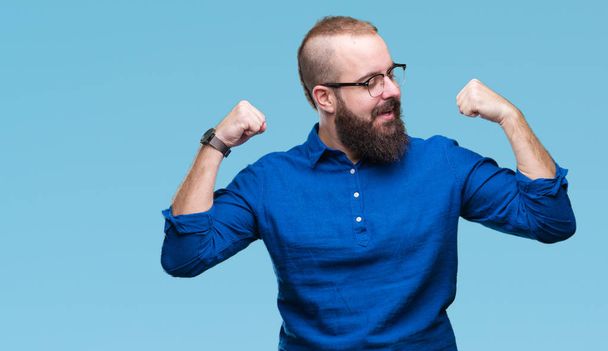 Homem jovem hipster caucasiano usando óculos sobre fundo isolado mostrando os músculos dos braços sorrindo orgulhoso. Conceito de aptidão
. - Foto, Imagem