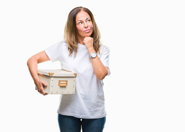 Mujer hispana de mediana edad moviéndose sosteniendo la caja de embalaje sobre fondo aislado cara seria pensando en la pregunta, idea muy confusa
 - Foto, imagen