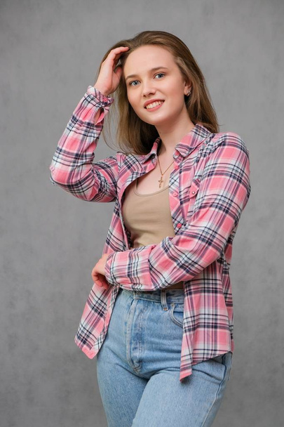 portrait of soncept young cheerful long-haired brunette woman in casual clothes in tight blue jeans and a checkered shirt. - Photo, Image