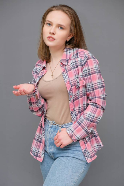 portrait of soncept young cheerful long-haired brunette woman in casual clothes in tight blue jeans and a checkered shirt. - Фото, зображення