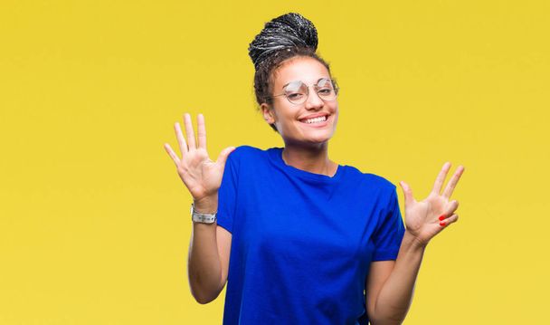 Jeune fille afro-américaine cheveux tressés portant des lunettes sur fond isolé montrant et pointant vers le haut avec les doigts numéro huit tout en souriant confiant et heureux
. - Photo, image