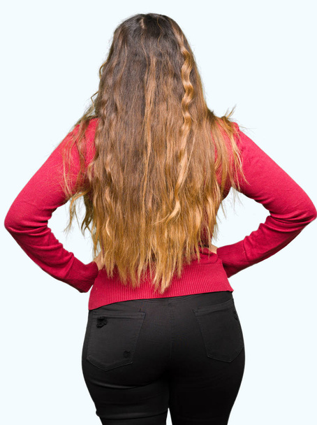 Fiatal szép nő visel piros pulóver állandó hátra keres el karral a test - Fotó, kép
