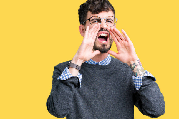Молодой красивый умный мужчина в очках на изолированном фоне кричит громко, с руками над ртом
 - Фото, изображение