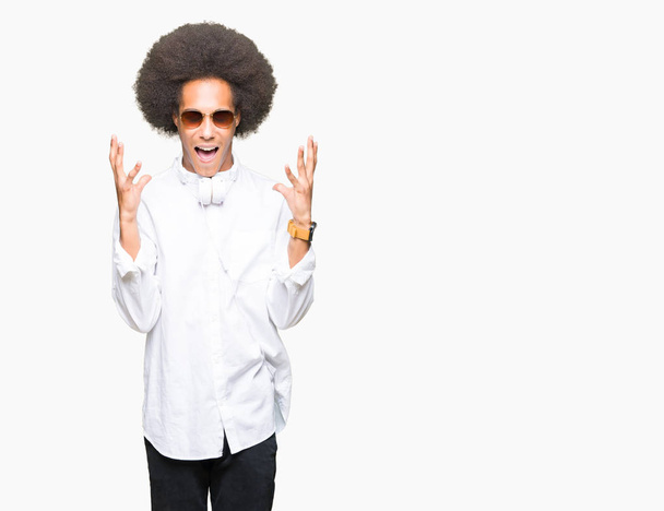 Young african american man with afro hair wearing sunglasses and headphones celebrating mad and crazy for success with arms raised and closed eyes screaming excited. Winner concept - Fotografie, Obrázek
