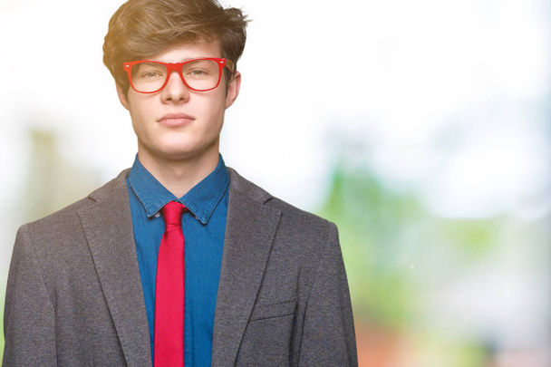 Young handsome business man wearing red glasses over isolated background with serious expression on face. Simple and natural looking at the camera. - Foto, Imagem