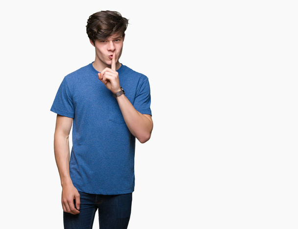 junger gutaussehender Mann in blauem T-Shirt vor isoliertem Hintergrund, der darum bittet, mit dem Finger auf den Lippen ruhig zu sein. Schweigen und geheimes Konzept. - Foto, Bild