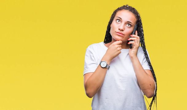 Genç örgülü saç Afro-Amerikan Kız gösteren arama smartphone izole arka plan ciddi bir yüz düşünme hakkında soru, çok karışık bir fikir üzerinde kullanma - Fotoğraf, Görsel