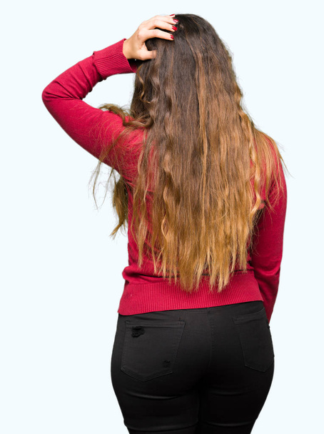 Young beautiful woman wearing red sweater Backwards thinking about doubt with hand on head - Fotoğraf, Görsel