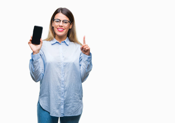 Молода красива бізнес-леді, показуючи порожній екран смартфона на ізольованому фоні, здивована ідеєю або питанням, що вказує пальцем щасливе обличчя, номер один
 - Фото, зображення