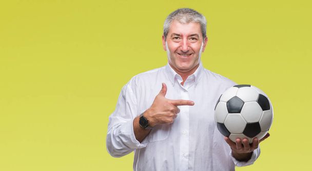 Bello uomo anziano che tiene palla da calcio su sfondo isolato molto felice che punta con mano e dito
 - Foto, immagini