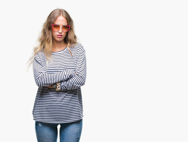 Beautiful young blonde woman wearing sunglasses over isolated background skeptic and nervous, disapproving expression on face with crossed arms. Negative person. - Фото, зображення