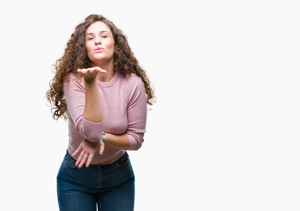 Beautiful brunette curly hair young girl wearing pink sweater over isolated background looking at the camera blowing a kiss with hand on air being lovely and sexy. Love expression. - Photo, Image