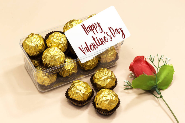vak van gouden premium chocolade snoepjes met gelukkige Valentijnsdag kaart, roze bloem voor Valentijnsdag vakantie - Foto, afbeelding