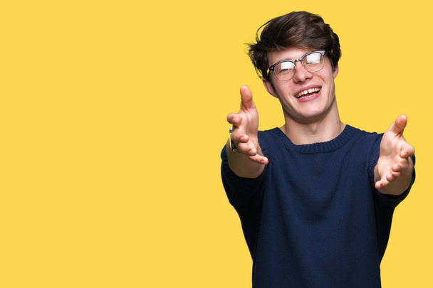 Mladý pohledný muž nosí brýle izolované pozadí pohledu na kameru s otevřenou náručí objetí úsměvem. Veselý výraz zahrnující štěstí. - Fotografie, Obrázek