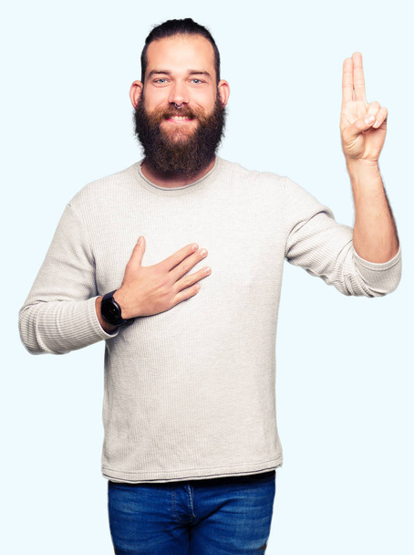 junger blonder Mann in lässigem Pullover, der mit der Hand auf Brust und Finger schwört und einen Treueschwur ablegt - Foto, Bild