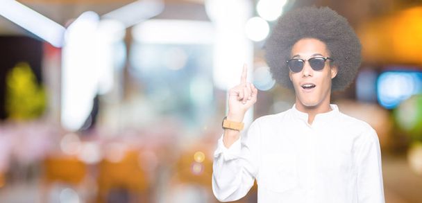Молодий афроамериканець людиною з афро волосся носити сонцезахисні окуляри, вказуючи пальцем з успішним ідеєю. Виходили і щасливі. Номер один. - Фото, зображення