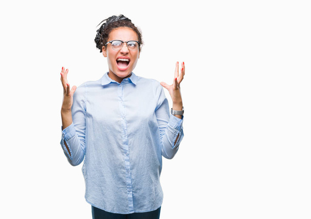 Young braided hair african american business girl wearing glasses over isolated background crazy and mad shouting and yelling with aggressive expression and arms raised. Frustration concept. - Photo, Image