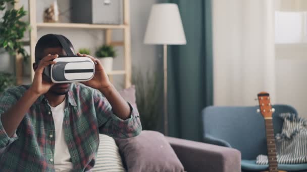 African American student is having fun with virtual reality glasses putting on device and moving arms relaxing at home enjoying modern technology and leisure time. - Séquence, vidéo