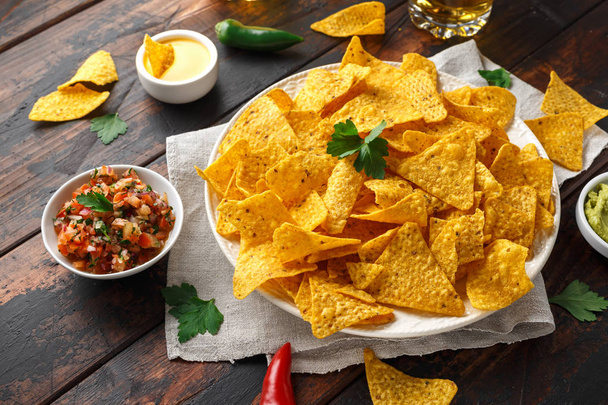 Tortilla nachos chips with cheese sauce, guacamole and tomatoes salsa dip. glass of beer. - Foto, Bild