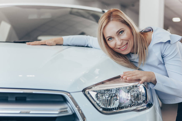 Happy mature woman embracing her new automobile after buying it at the dealership salon, copy space. Excited mid-aged businesswoman celebrating buying new auto. Success, comfort, transport concept - Photo, image