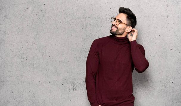 Handsome man with glasses thinking an idea while scratching head over textured wall - Fotoğraf, Görsel