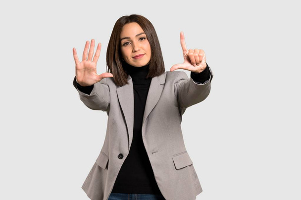 Joven mujer de negocios contando siete con dedos sobre fondo gris aislado
 - Foto, Imagen