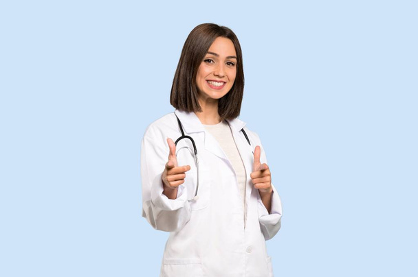 Молодая женщина доктор указывает пальцем на вас, улыбаясь на изолированном синем фоне
 - Фото, изображение