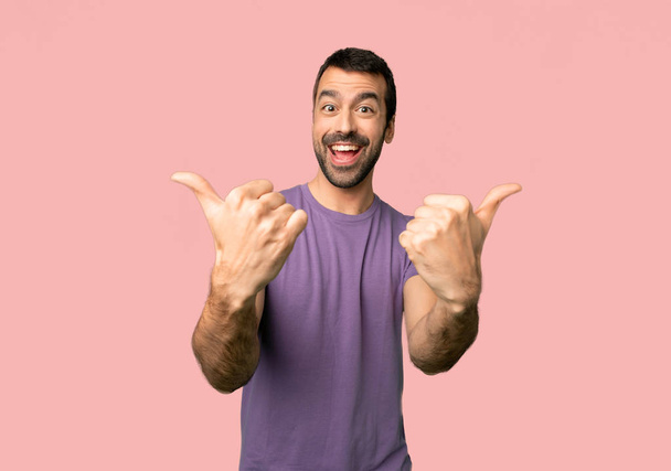 Knappe man het geven van een thumbs up gebaar met beide handen en glimlachend op geïsoleerde roze achtergrond - Foto, afbeelding