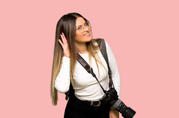 Nuori valokuvaaja nainen kuuntelee jotain laittamalla käsi korvaan eristetty vaaleanpunainen tausta
 - Valokuva, kuva