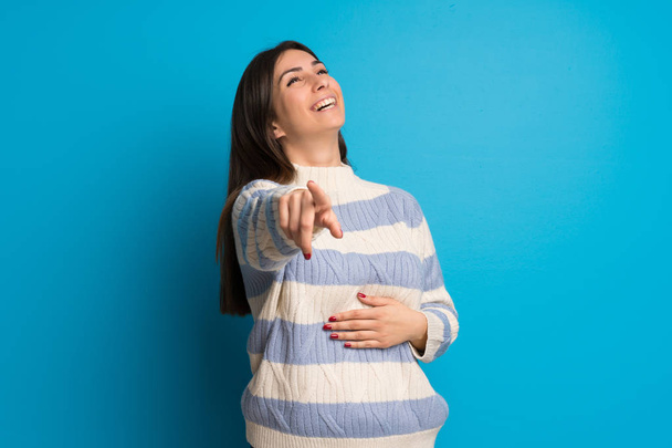 Młoda kobieta nad niebieską ścianę wskazując palcem na kogoś i śmiejąc się dużo - Zdjęcie, obraz