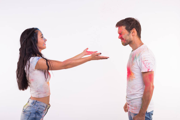 Dovolená, holi a lidé koncept - šťastný pár se baví s vícebarevné prášek na jejich tvářích na bílém pozadí - Fotografie, Obrázek