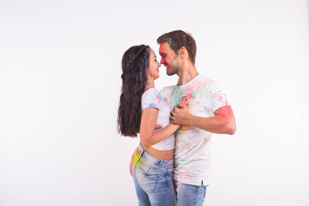 Holiday, social dance, holi and people concept - Happy couple having fun and dancing bachata or kizomba with multicolored powder on their faces on white background with copy space - Photo, Image