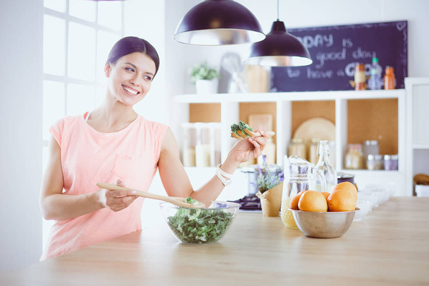 Улыбающаяся молодая женщина смешивает свежий салат на кухне. - Фото, изображение